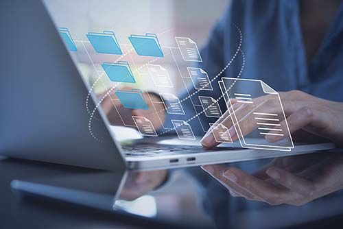 Image of woman typing on laptop while digital images of files and documents float on screen